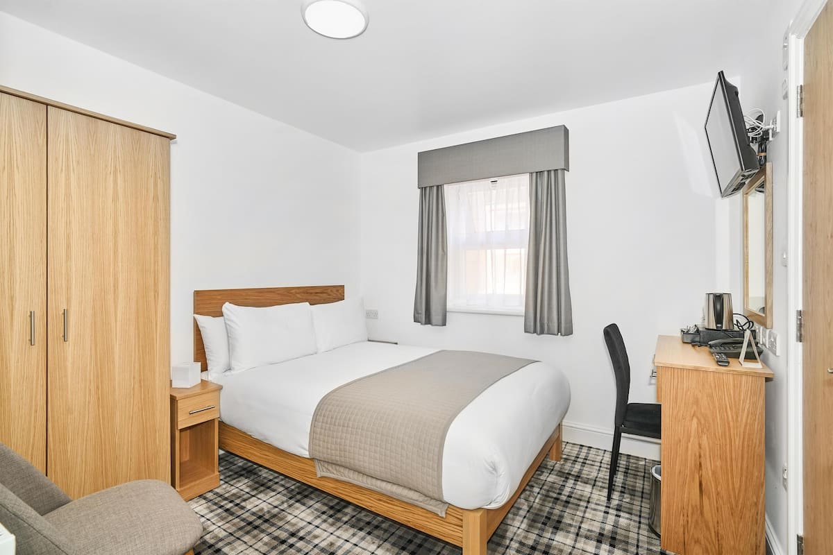 A hotel room with a bed, a desk, a chair, a wardrobe, and a television.