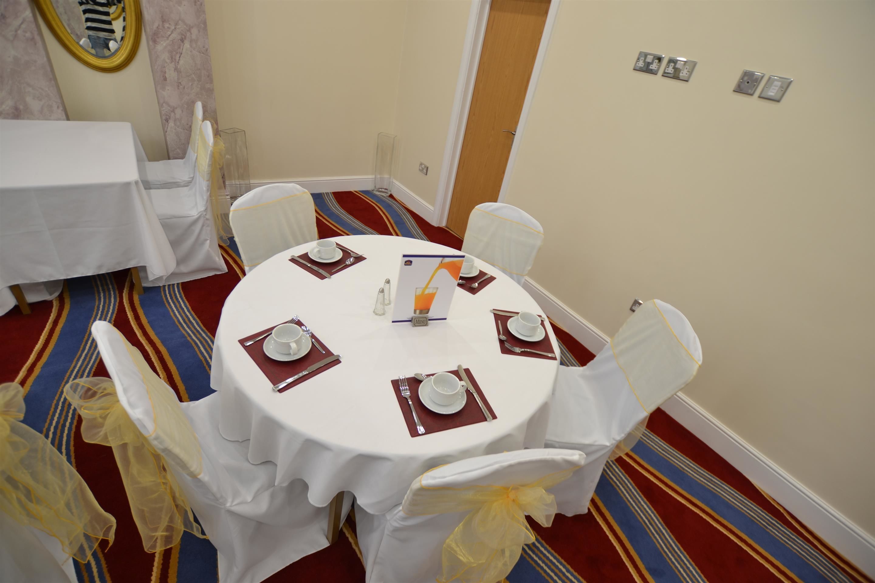 A round dining table with white tablecloth and chairs, set with plates, cutlery, and napkins.