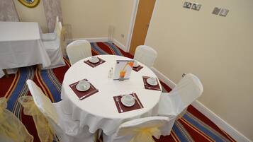 A round dining table with white tablecloth and chairs, set with plates, cutlery, and napkins.