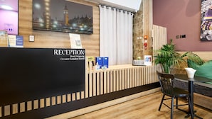 A reception desk with a cityscape poster, a sign for the conference hall, and a reception area with a plant and a table.