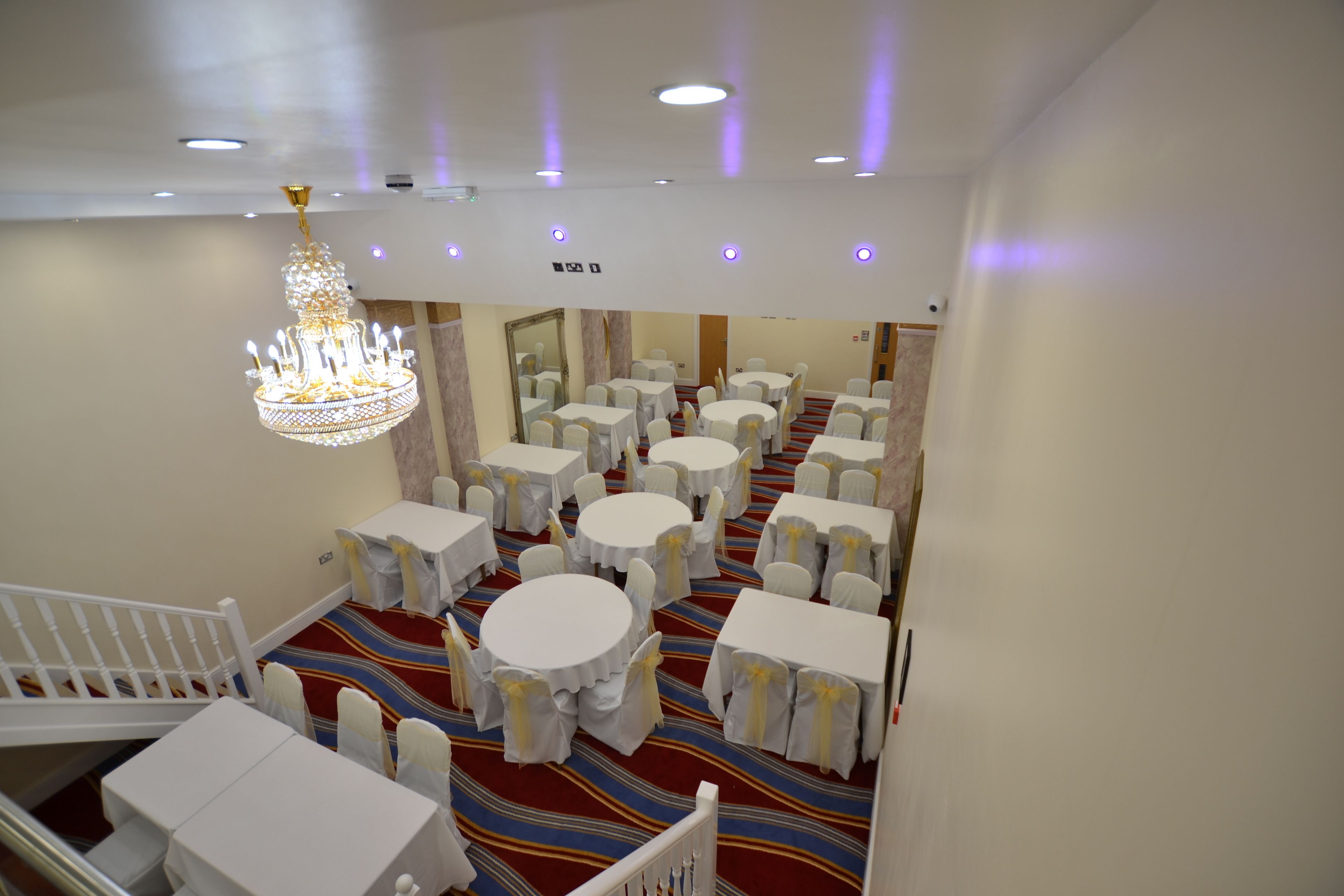 A hotel room with a large chandelier, multiple round tables with chairs, and a striped carpet.