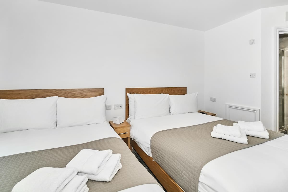 A hotel room with two beds, a wooden headboard, white bedding, and a visible power outlet.