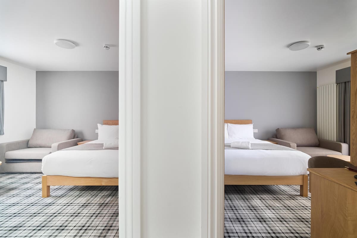 A modern hotel room with a large bed, a sofa, a desk, and a mirror.