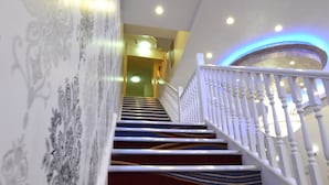 A staircase with a patterned carpet and white railings, leading to a landing with a light fixture.