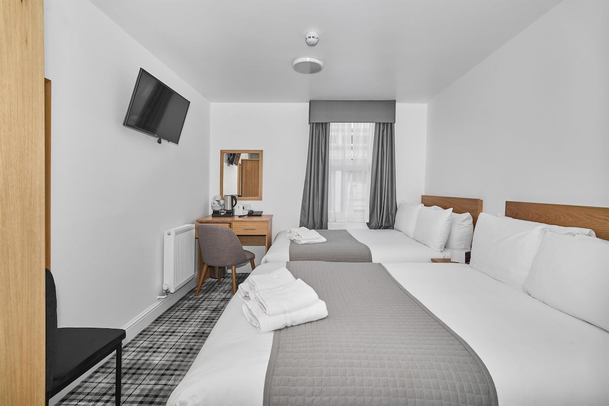 A hotel room with two beds, a desk with a chair, a television, and a window with curtains.