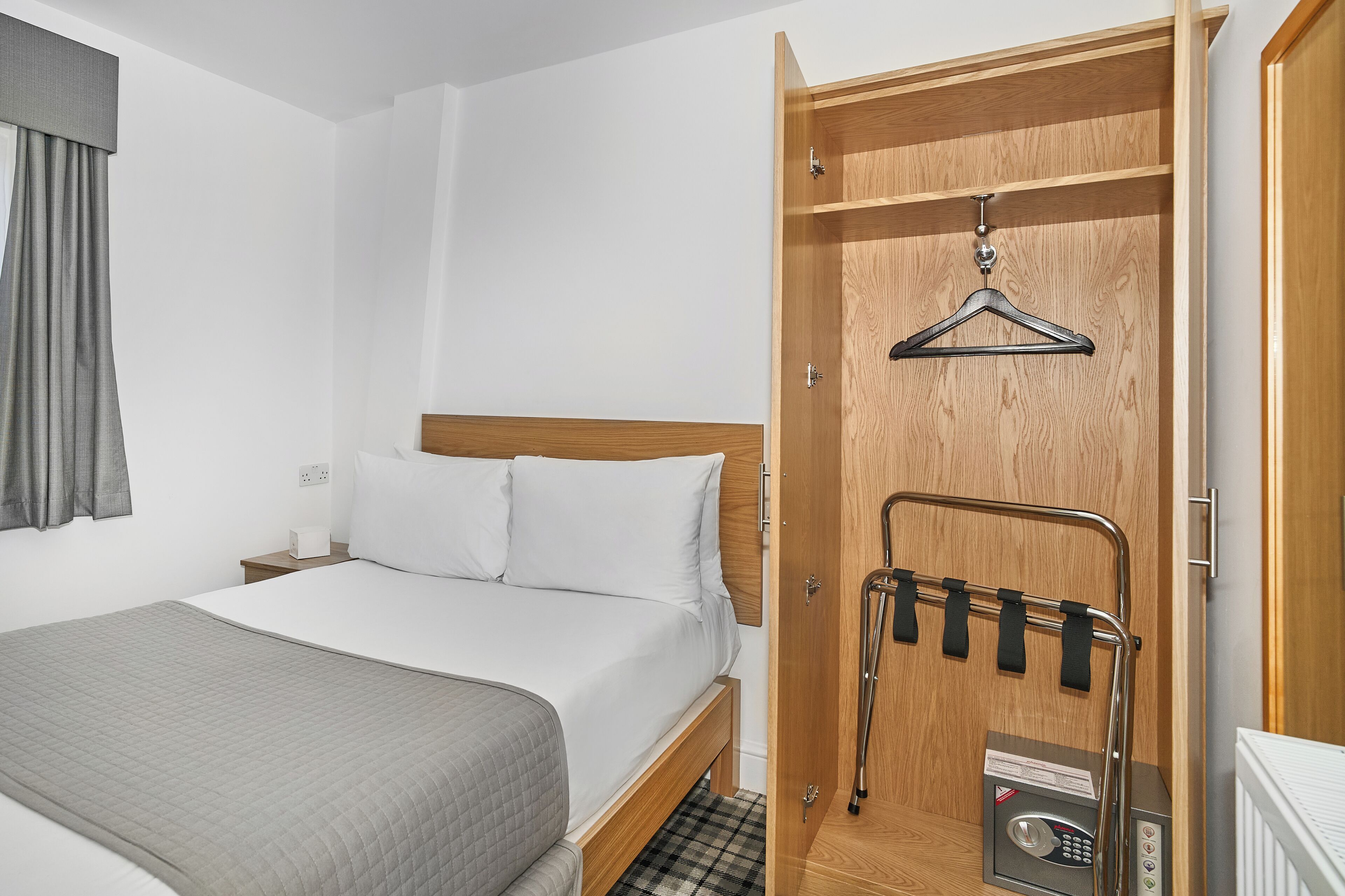 A hotel room with a bed, a wooden wardrobe, and a coat rack.