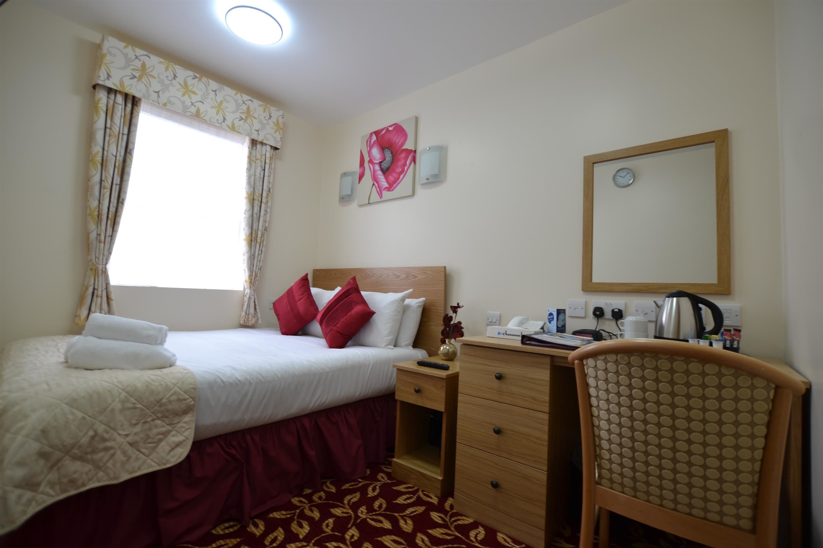A hotel room with a bed, a desk, a chair, a mirror, a clock, and a window with curtains.