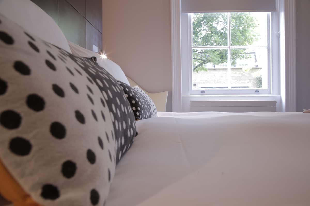 A bed with polka dot pillows, a window with a view of trees, and a white wall.