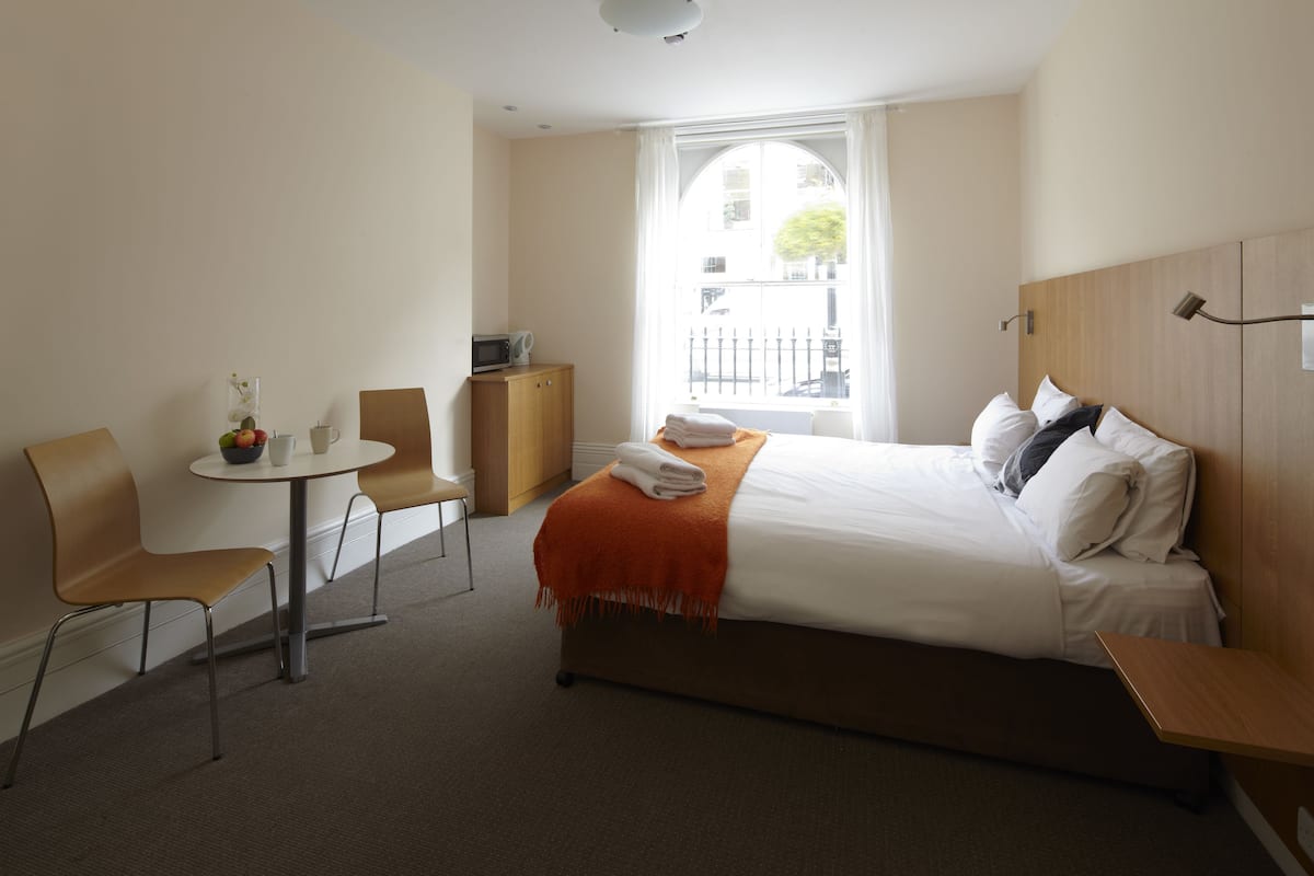 A hotel room with a bed, a small table with chairs, a window with a view of the street, and a cabinet.