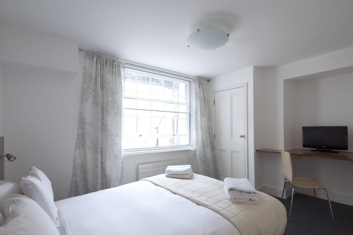 A hotel room with a large bed, a desk with a television, and a window with curtains.