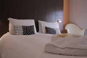 A neatly made bed with white and polka-dotted pillows, a white headboard, and a folded white towel on the bed. - B+B Belgravia (London)