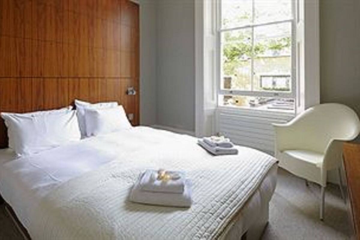 A hotel room with a large bed, a wooden headboard, a window with a view, and a white chair.