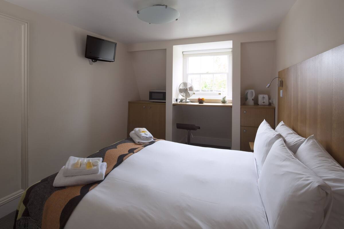 A hotel room with a large bed, a desk with a computer, a television, and a window with a view of the outdoors.
