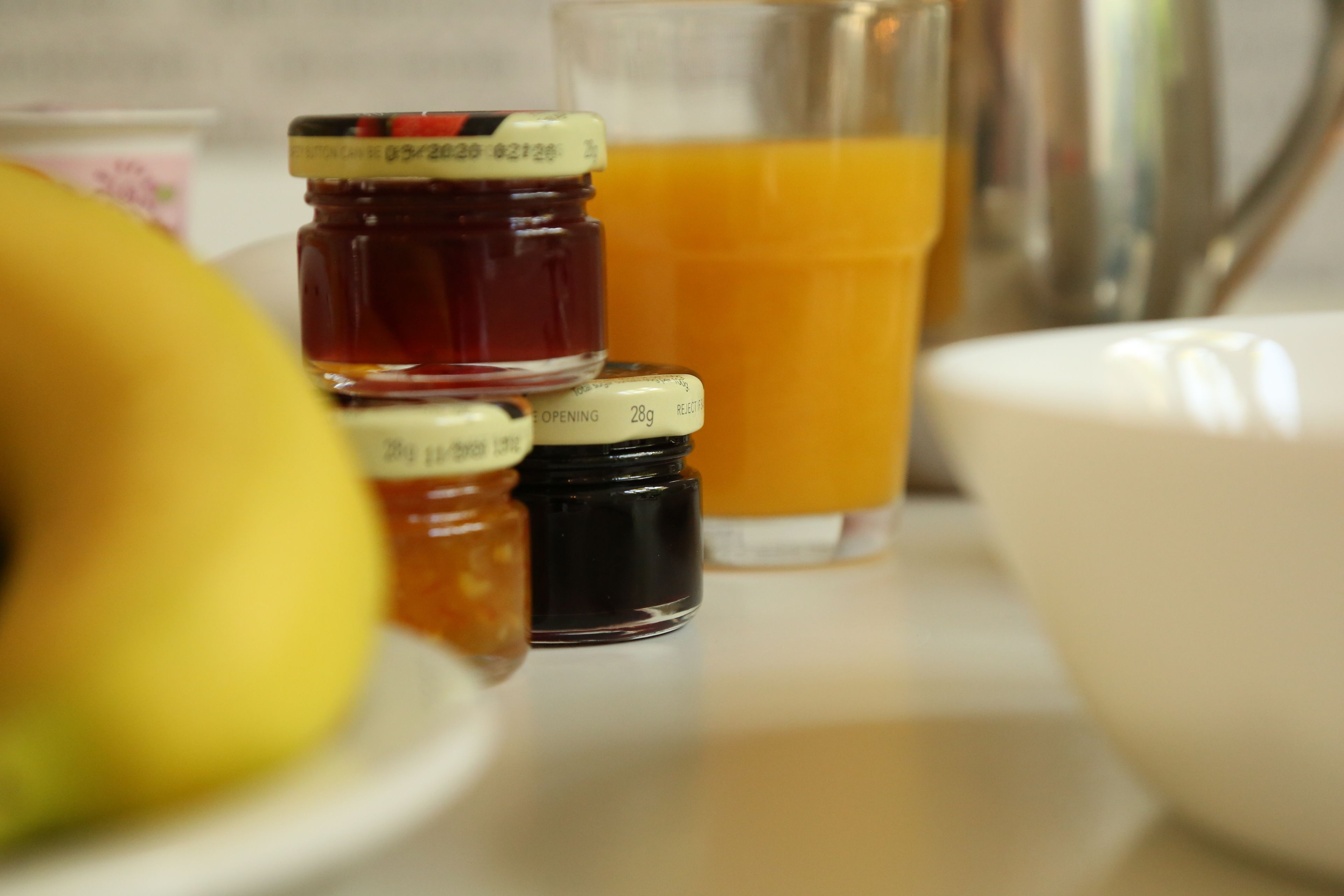 A table with jars of condiments, a glass of orange juice, and a bowl.