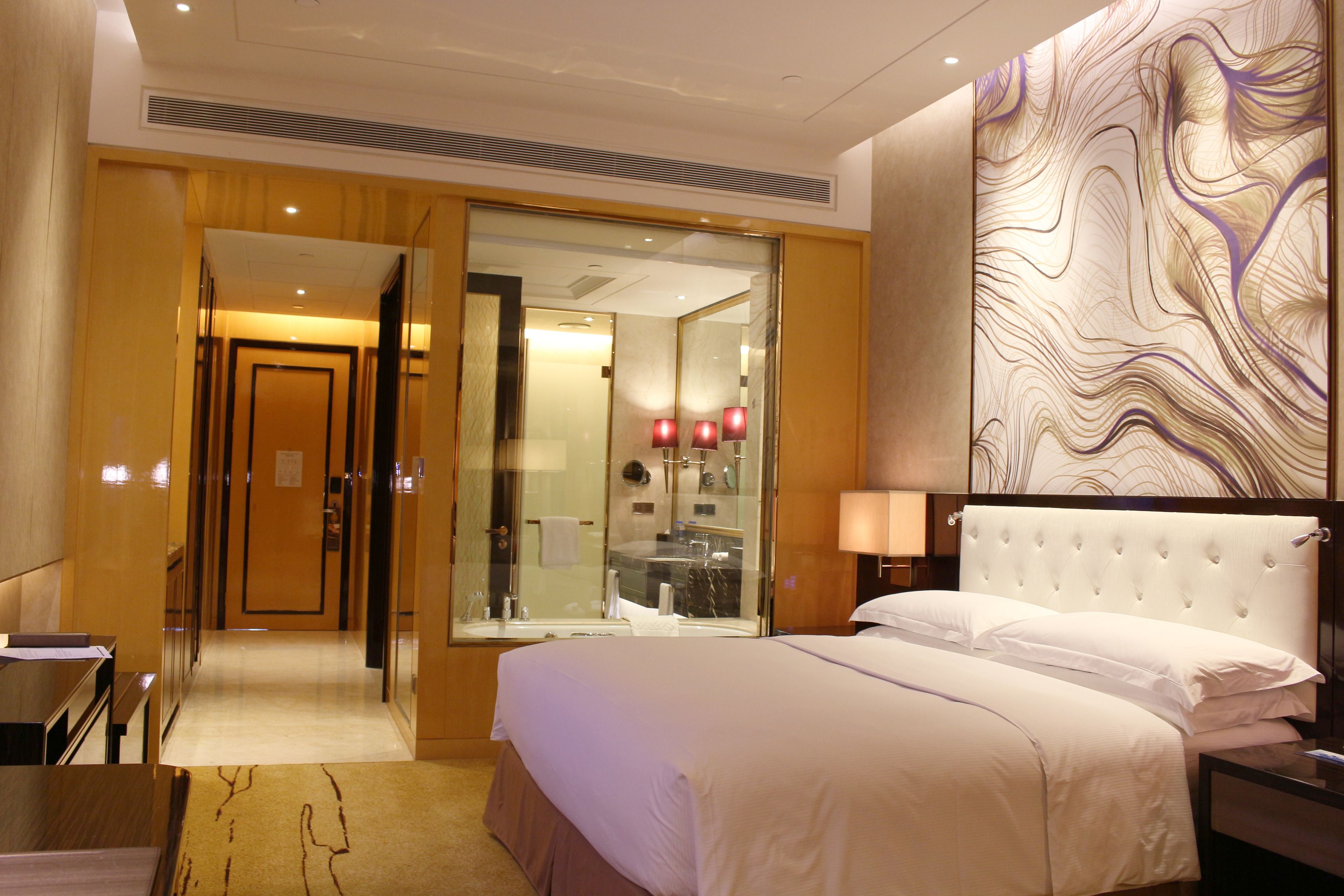 A hotel room with a large bed, a glass-enclosed bathroom, and a modern wall design.