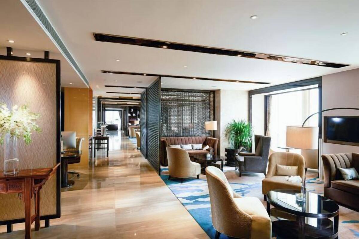 Un hall d’hôtel moderne avec un long couloir, un espace détente avec des canapés et des fauteuils, un téléviseur et une grande fenêtre.
