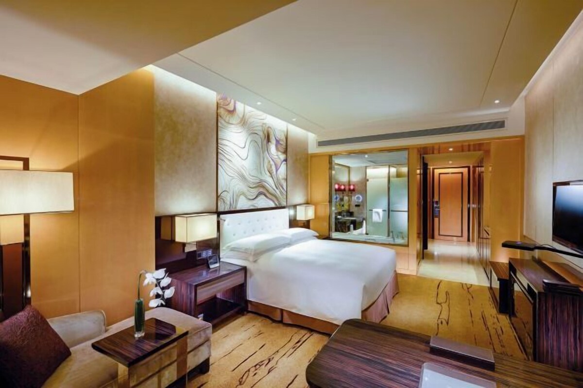 A hotel room with a bed, bedside tables, a TV, a sofa, and a mirror.