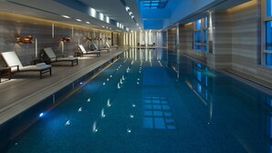 A modern indoor swimming pool with lounge chairs and a skylight. - Hilton Zhengzhou (Zhengzhou)