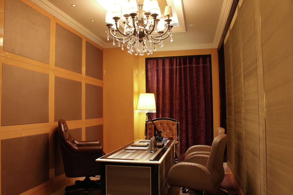 Une chambre d’hôtel équipée d’un bureau, de deux chaises, d’une lampe et d’un lustre.