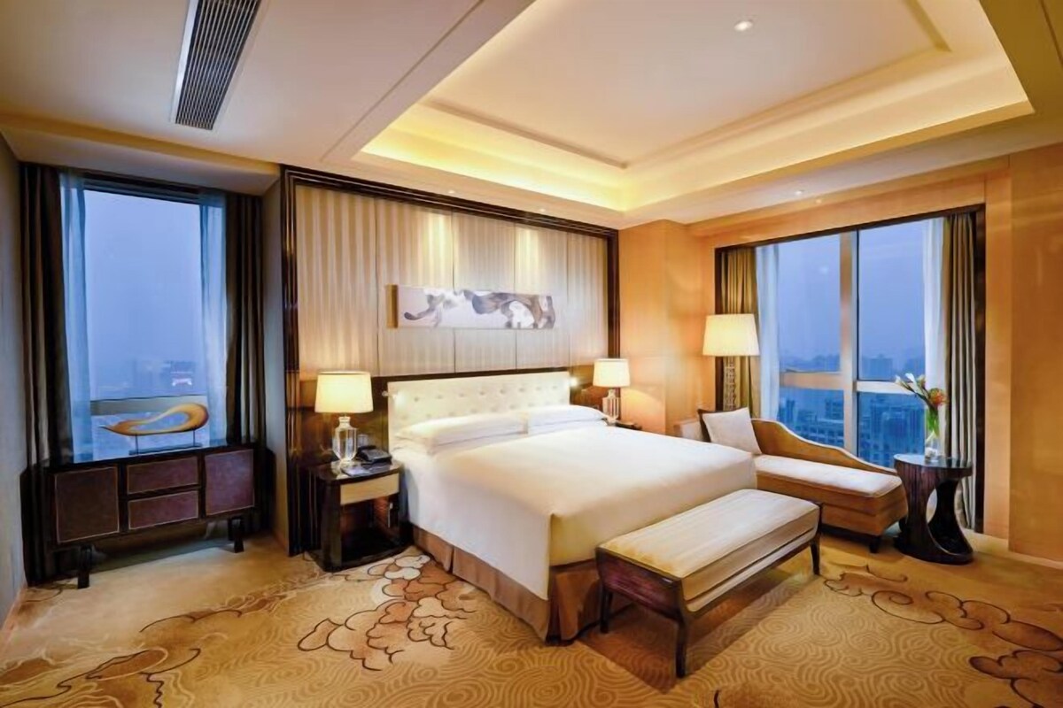 A hotel room with a large bed, a desk, a chair, and a view of the city.