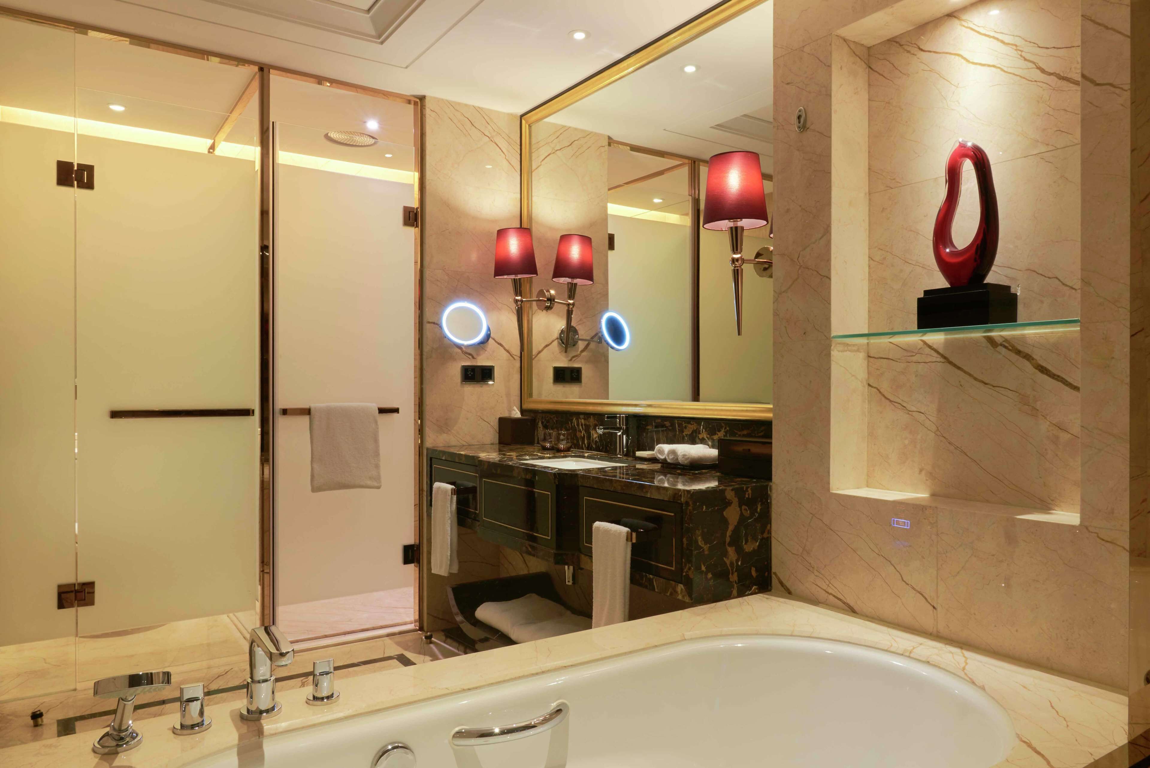 A modern bathroom with a large mirror, a bathtub, two sinks, and a vanity with a marble countertop.
