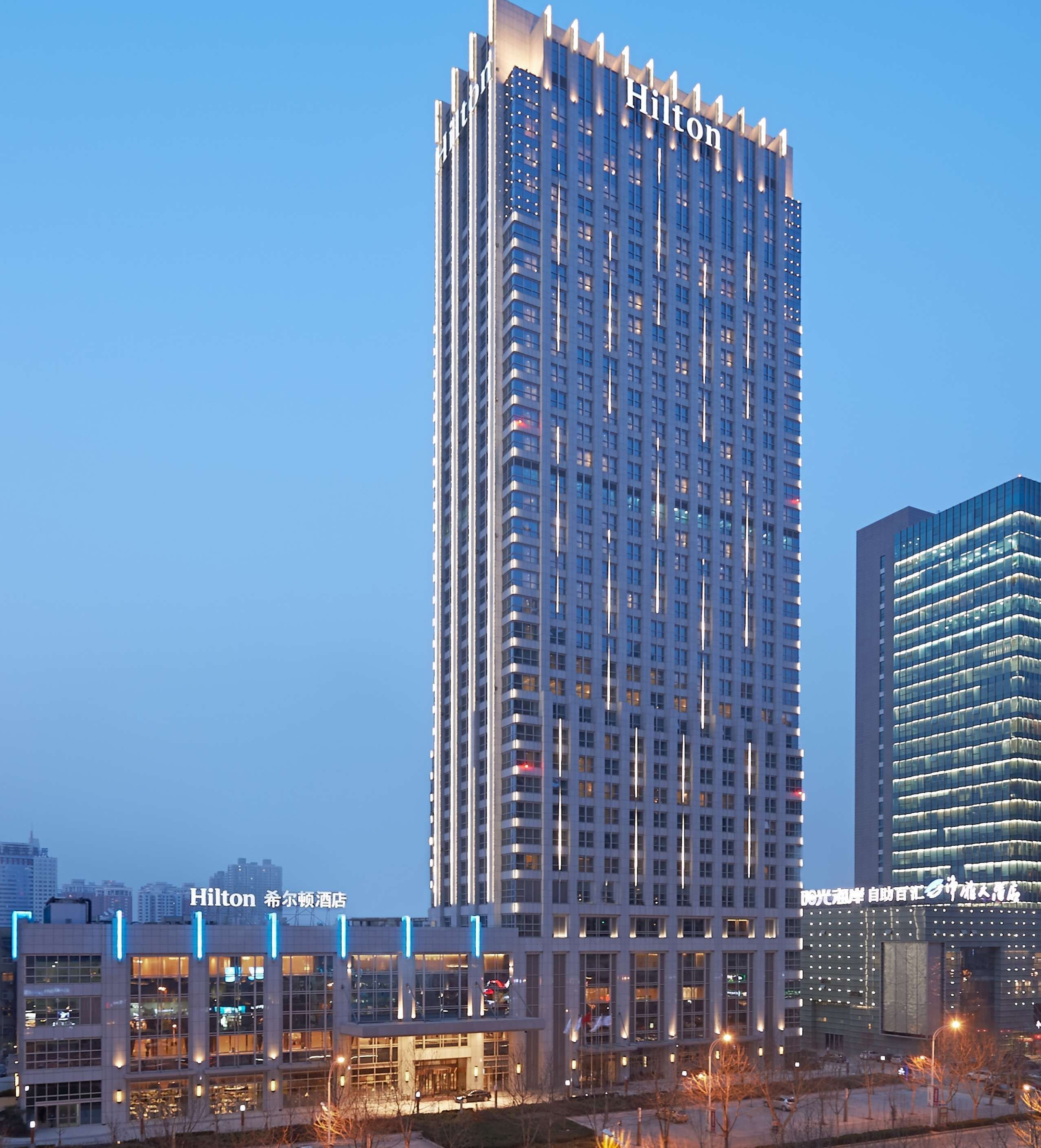 Een hoog hotelgebouw met een modern ontwerp, met een groot 'Hilton' bord bovenaan.