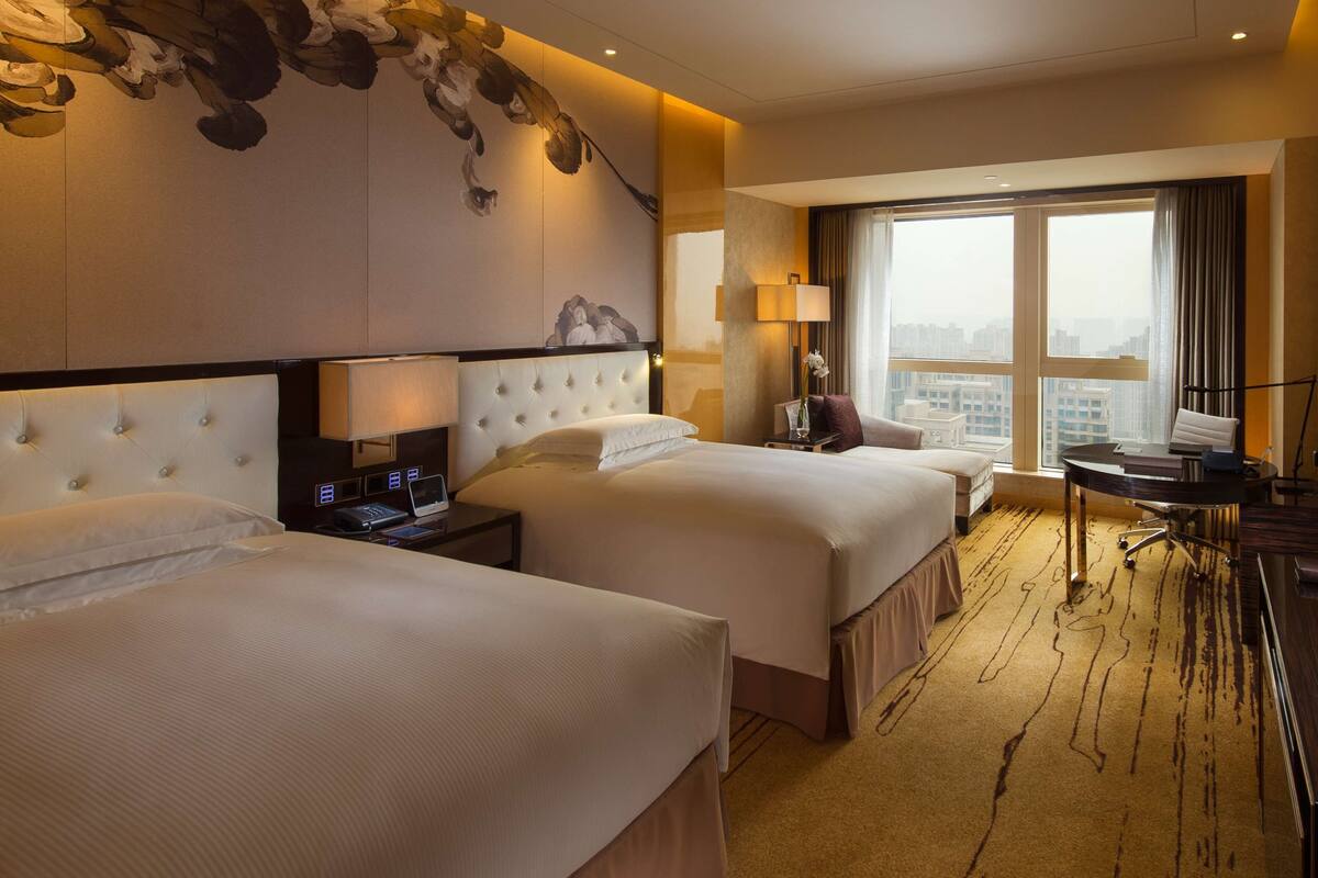 Une chambre d’hôtel avec deux lits, un bureau et une grande fenêtre donnant sur la ville.