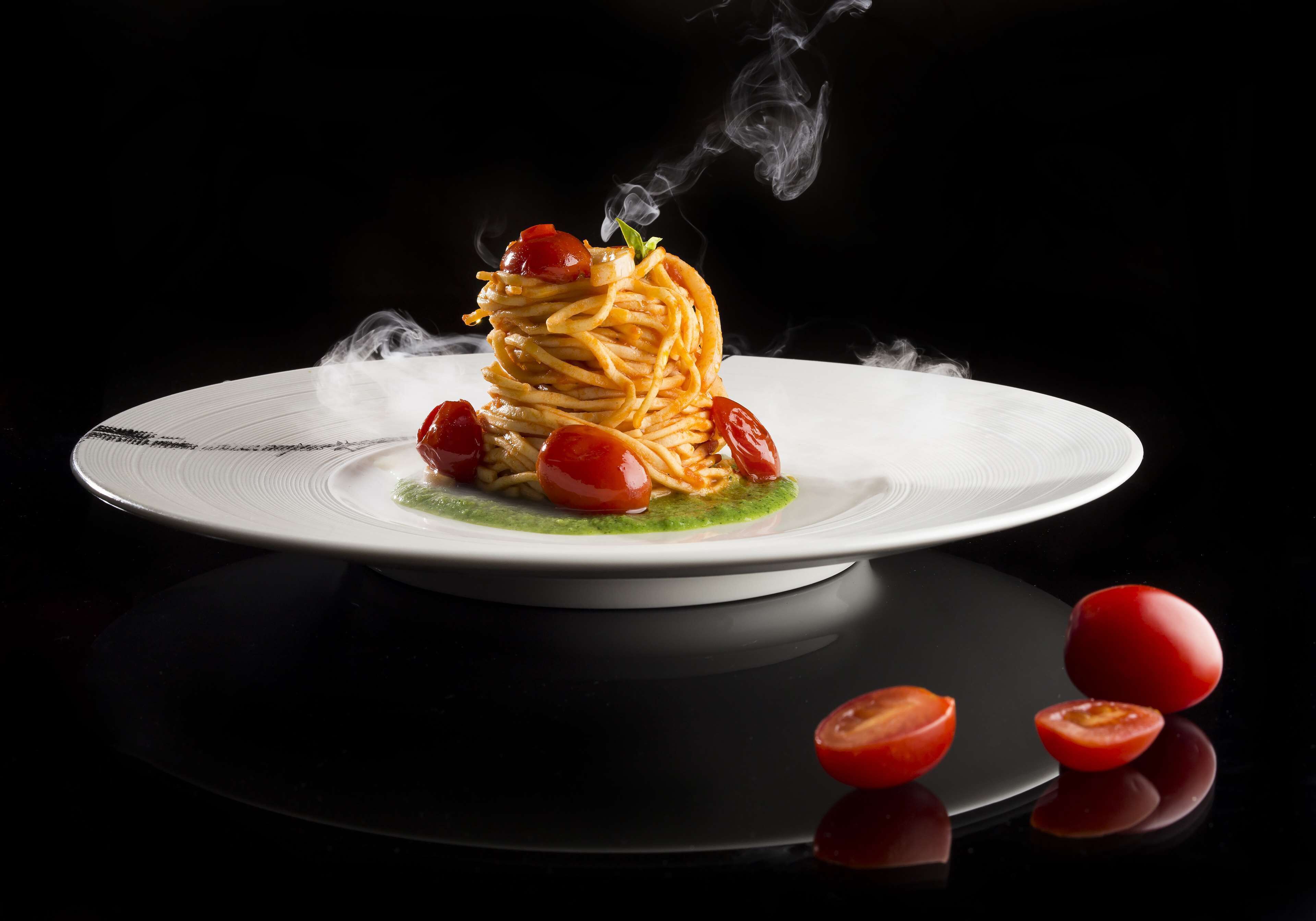 A plate of spaghetti with cherry tomatoes and a green sauce, steam rising from the dish.