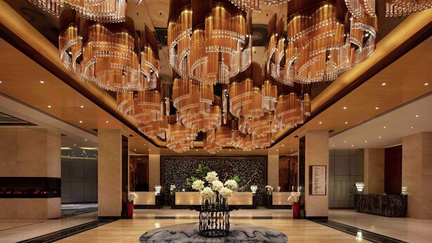 A spacious lobby with a central reception desk, multiple chandeliers, and a marble floor. - Hilton Zhengzhou (Zhengzhou)