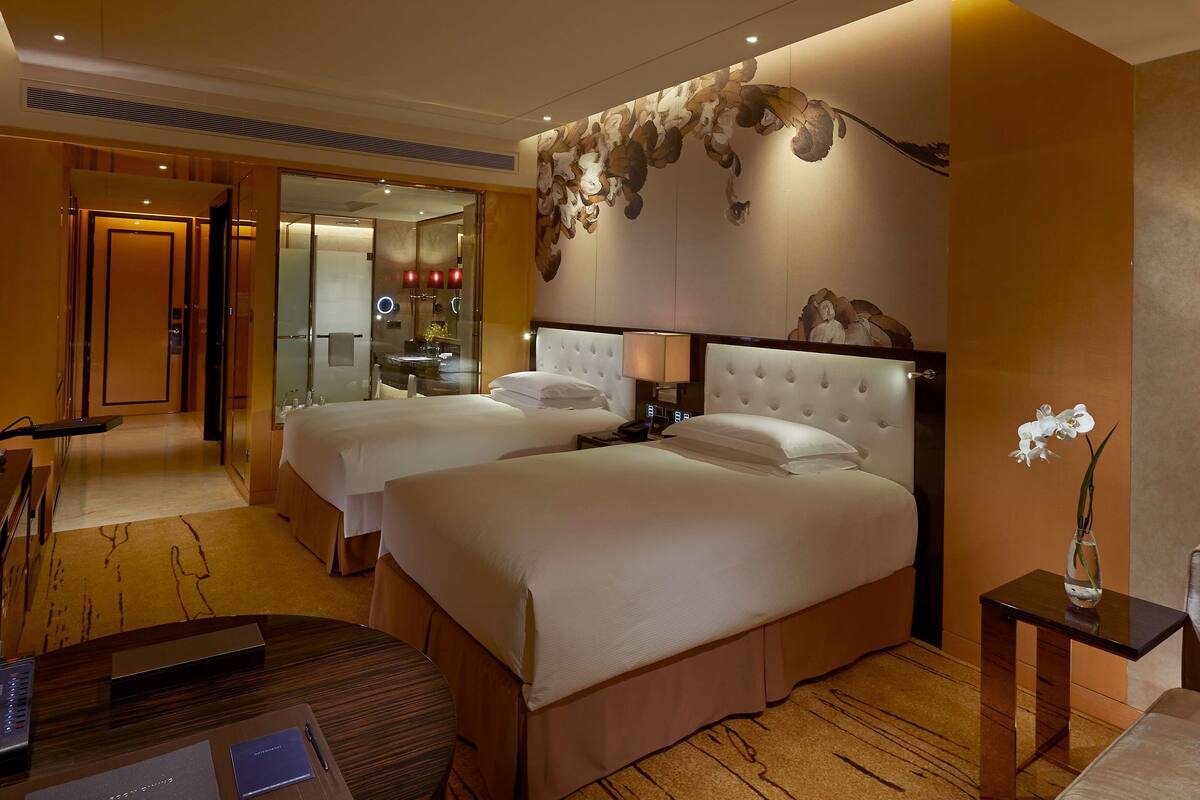 Une chambre d’hôtel avec deux lits, un bureau et une salle de bain visible à travers une porte ouverte.