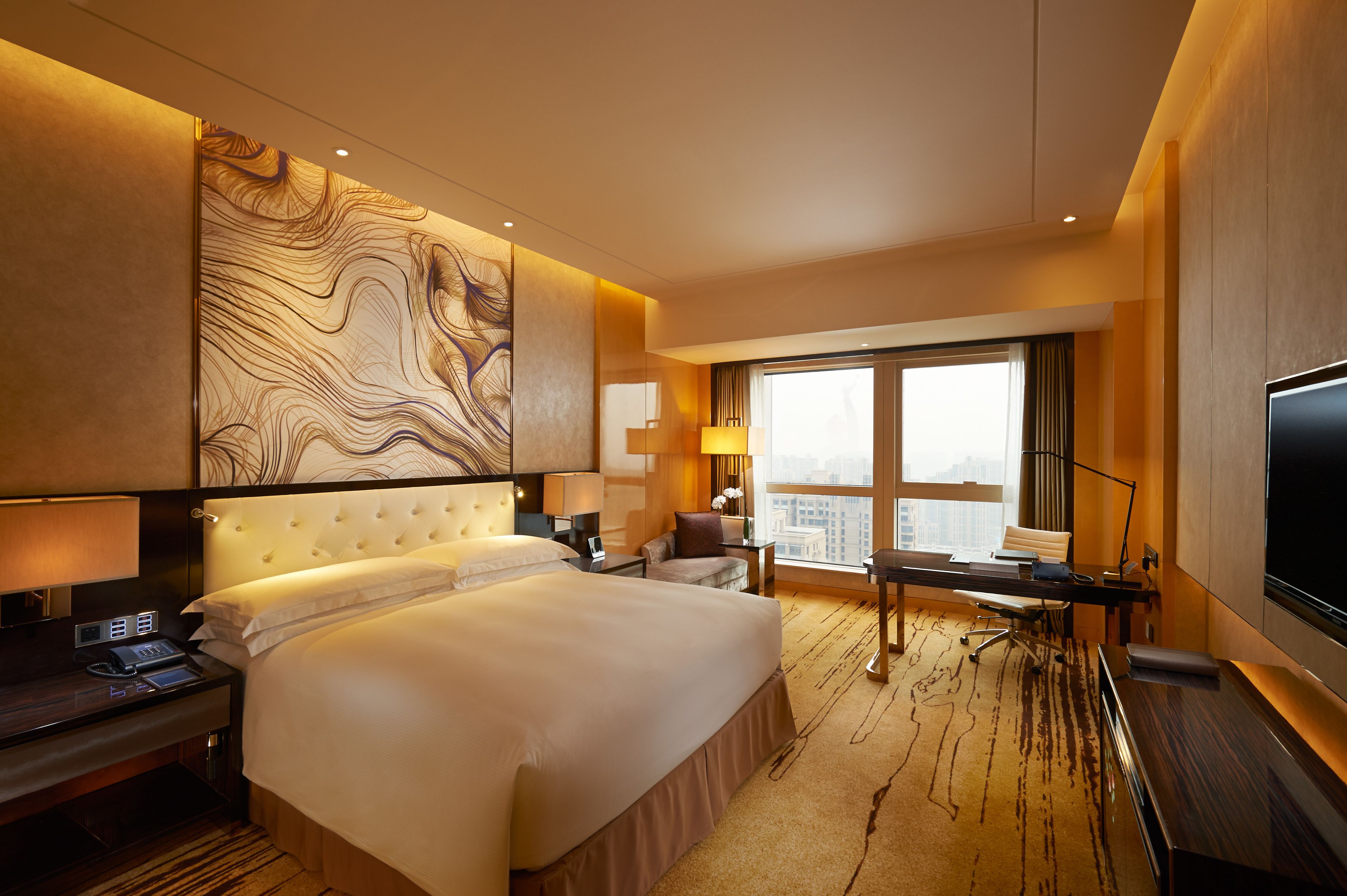 Een moderne hotelkamer met een groot bed, een bureau, een stoel, een televisie en uitzicht over de stad.