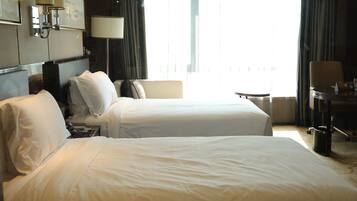 A hotel room with two beds, a desk, a chair, and a view of the outdoors.