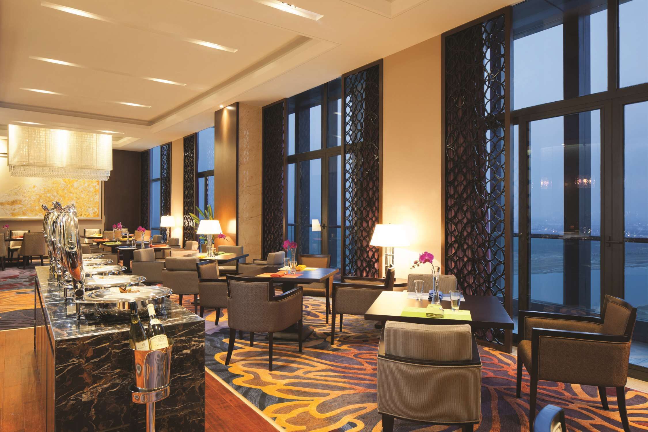 A hotel lobby with a marble reception desk, seating area, and large windows offering a view of the cityscape.