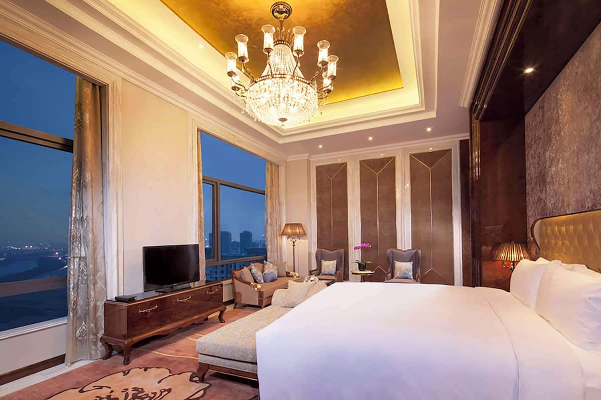 A spacious bedroom with a large bed, a television, and a view of the cityscape.
