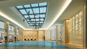 An indoor swimming pool with a skylight, seating area, and a city view.