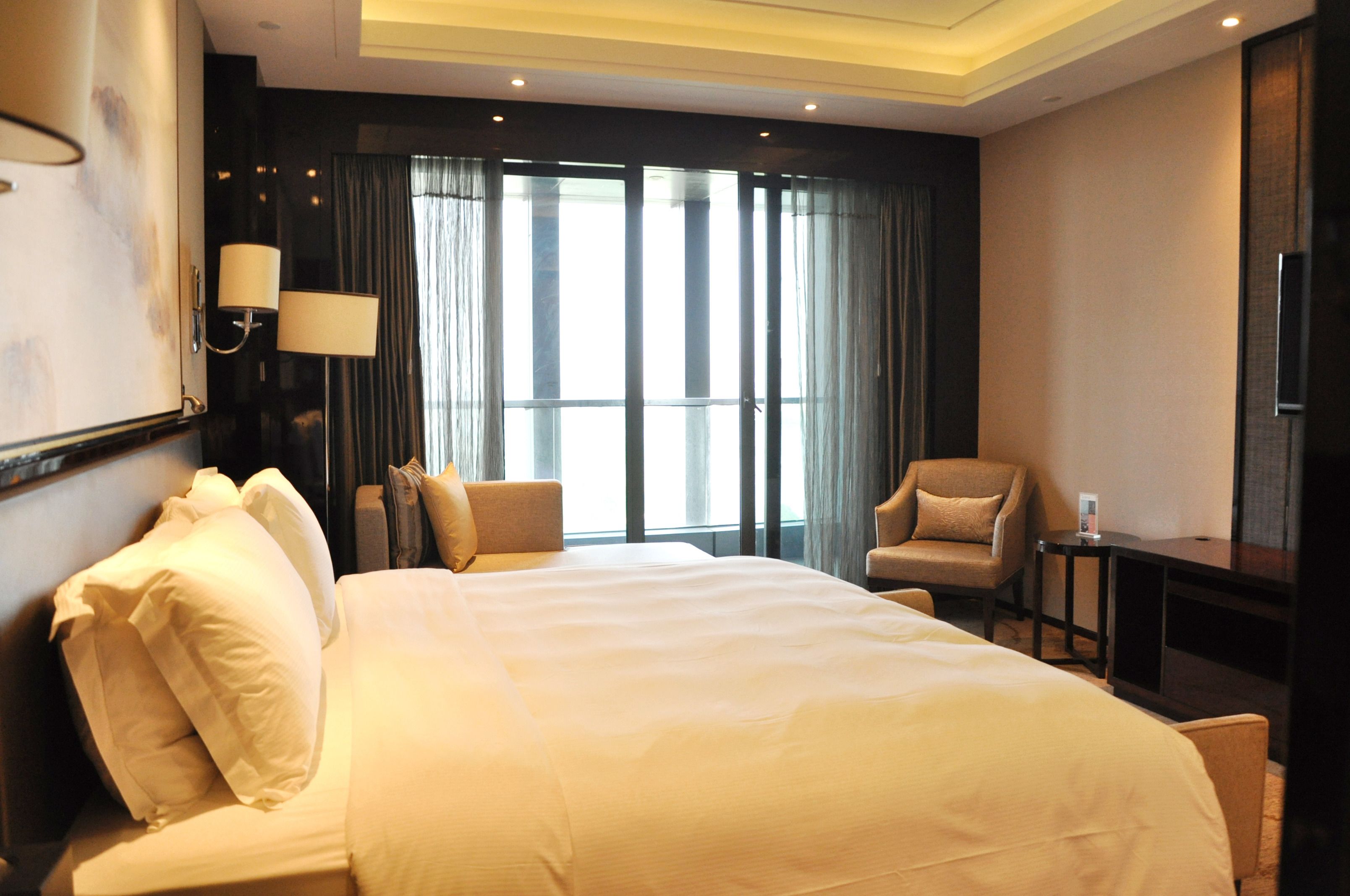 A hotel room with a large bed, two armchairs, a small table, and a TV.