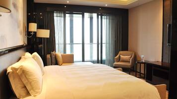 A hotel room with a large bed, two armchairs, a small table, and a TV.