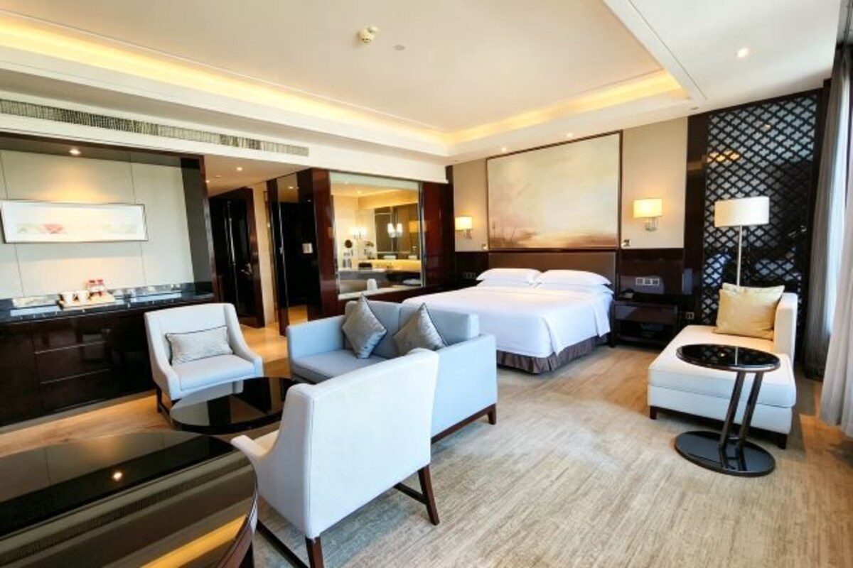 A hotel room with a bed, two armchairs, a sofa, a small table, and a desk with a chair.
