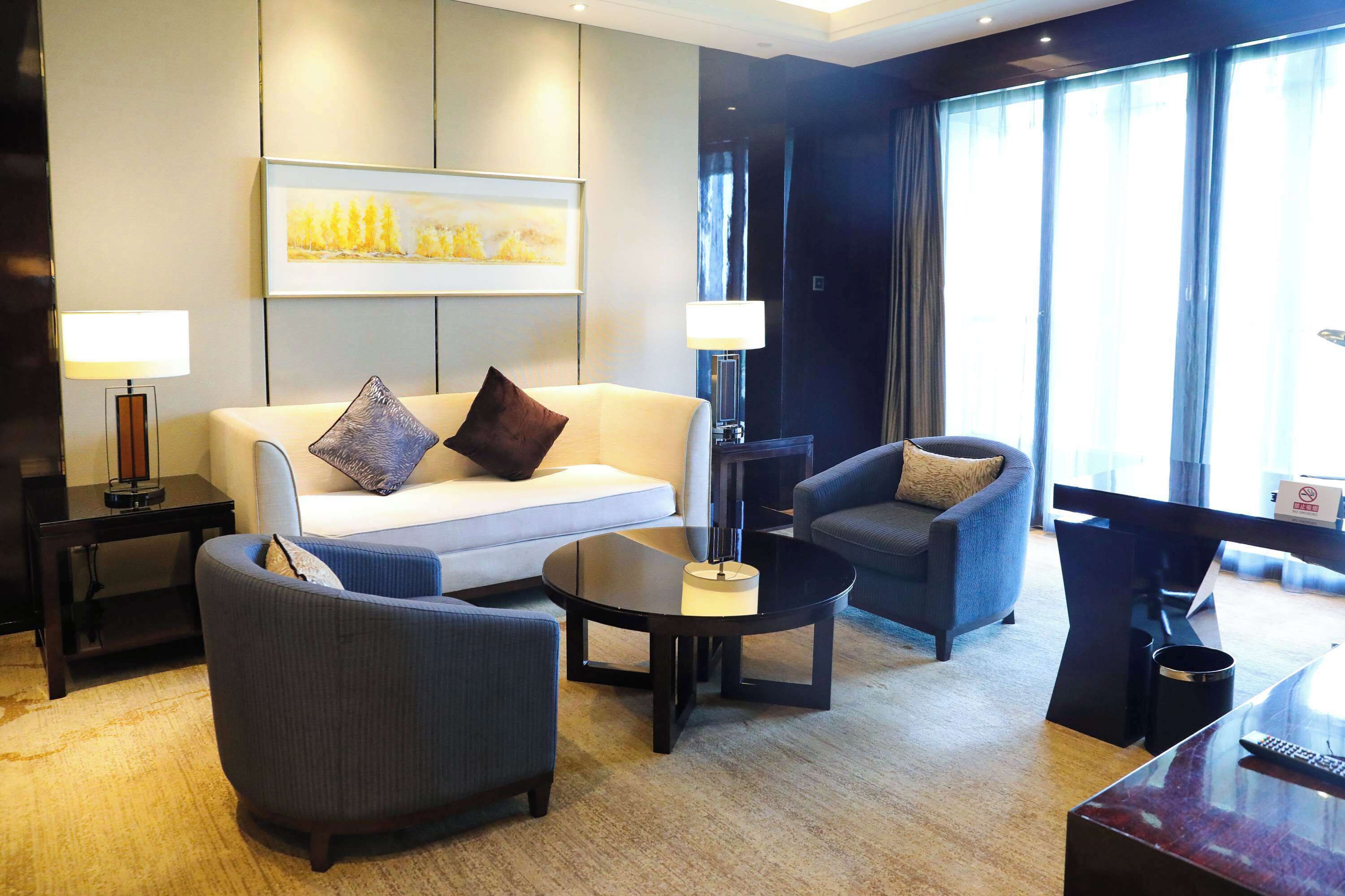 Una habitación de hotel moderna con sofá, dos sillones, una mesa de centro y un escritorio con lámpara.