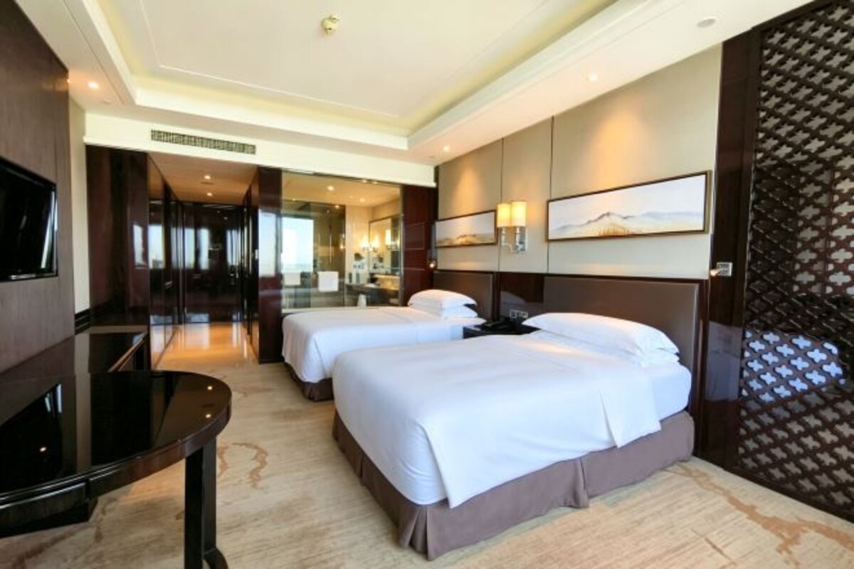 A hotel room with two beds, a TV, a desk, and a large window.
