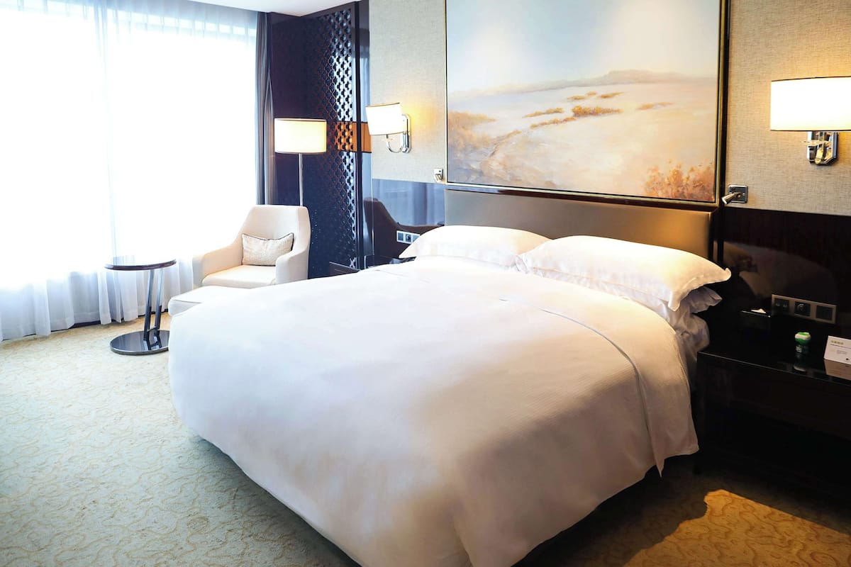 A hotel room with a large bed, a chair, a desk, and a painting on the wall.