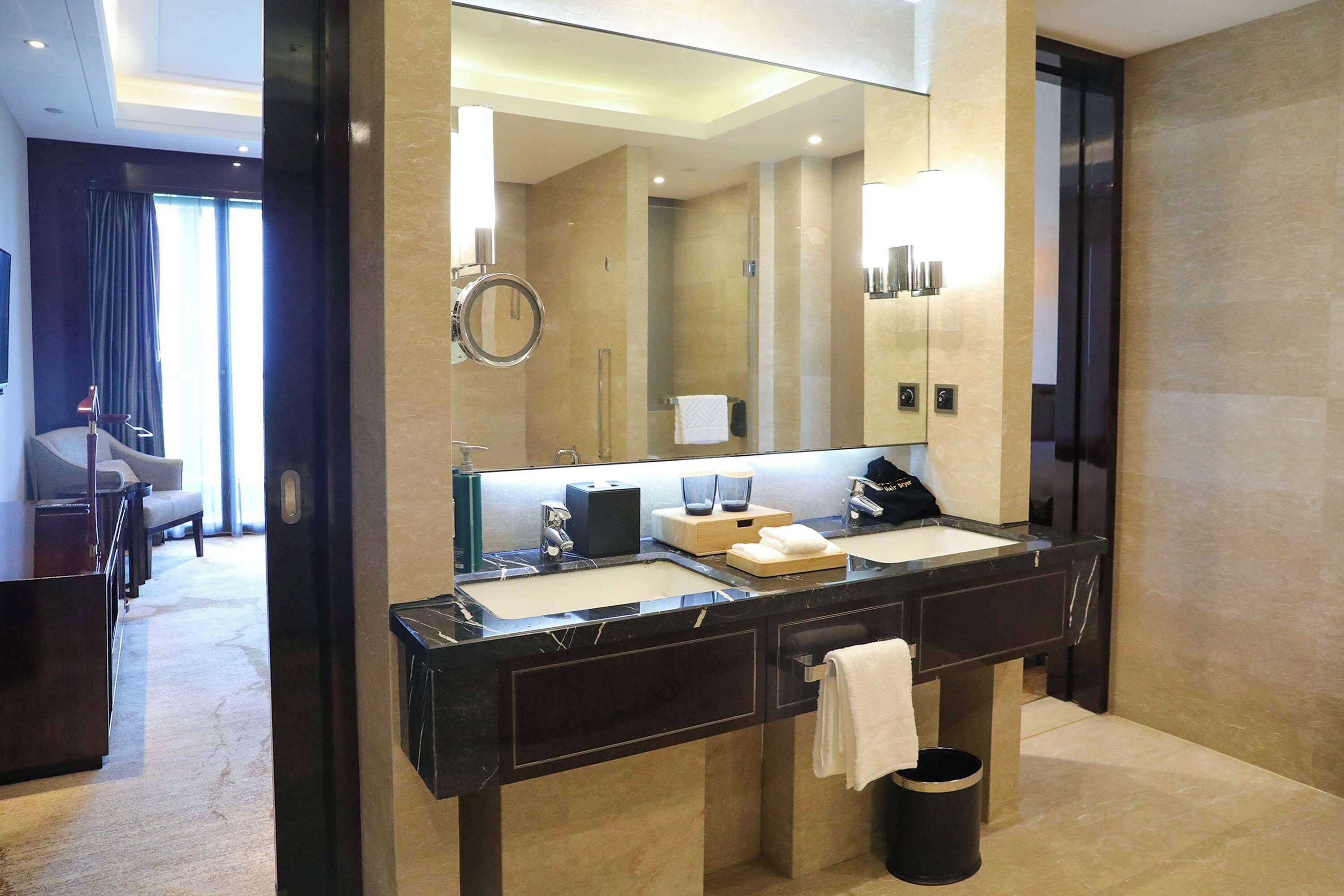 Un baño moderno con un espejo grande, lavamanos dobles y un cubo de basura negro.