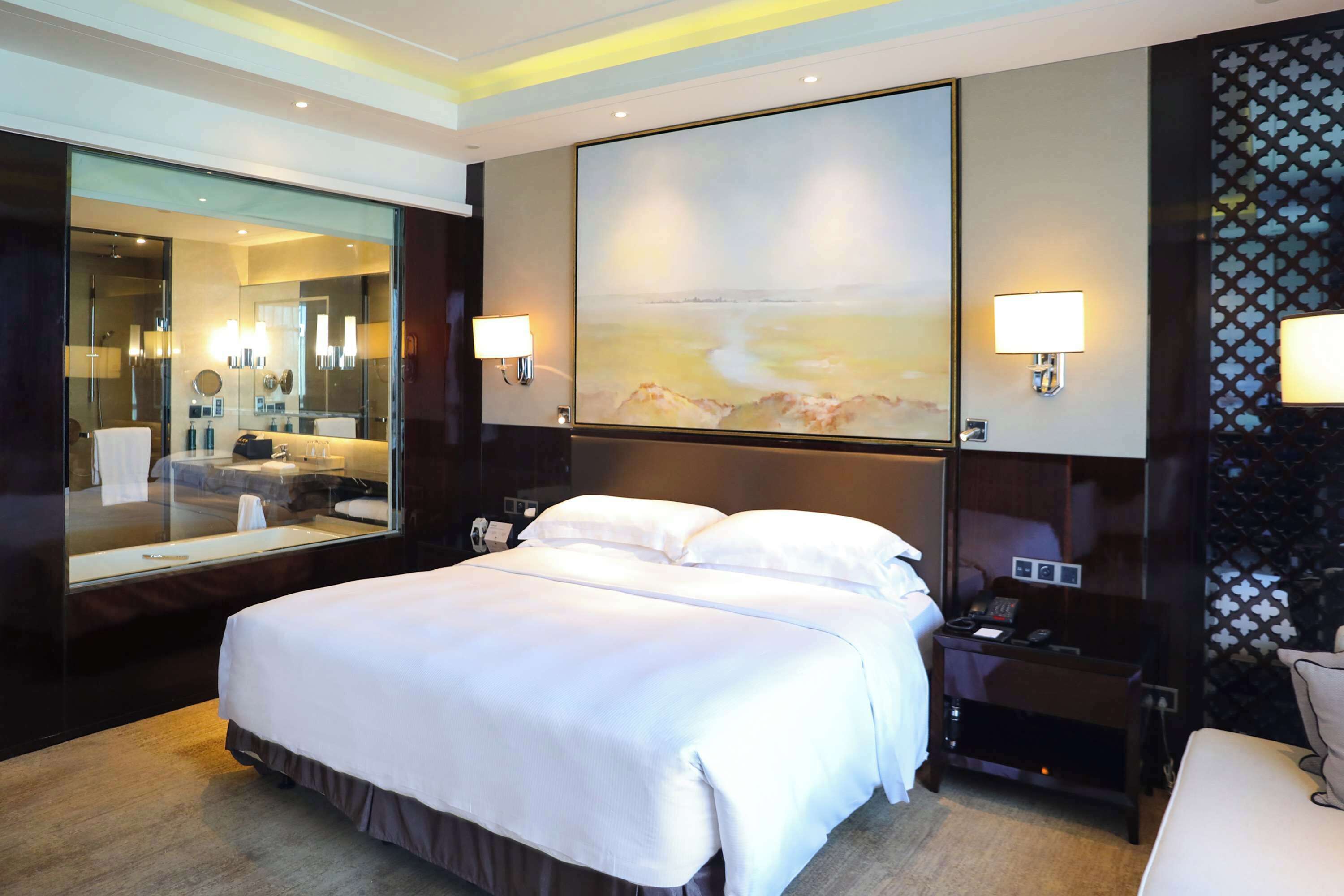 A hotel room with a large bed, a mirror, a painting, and two bedside lamps.