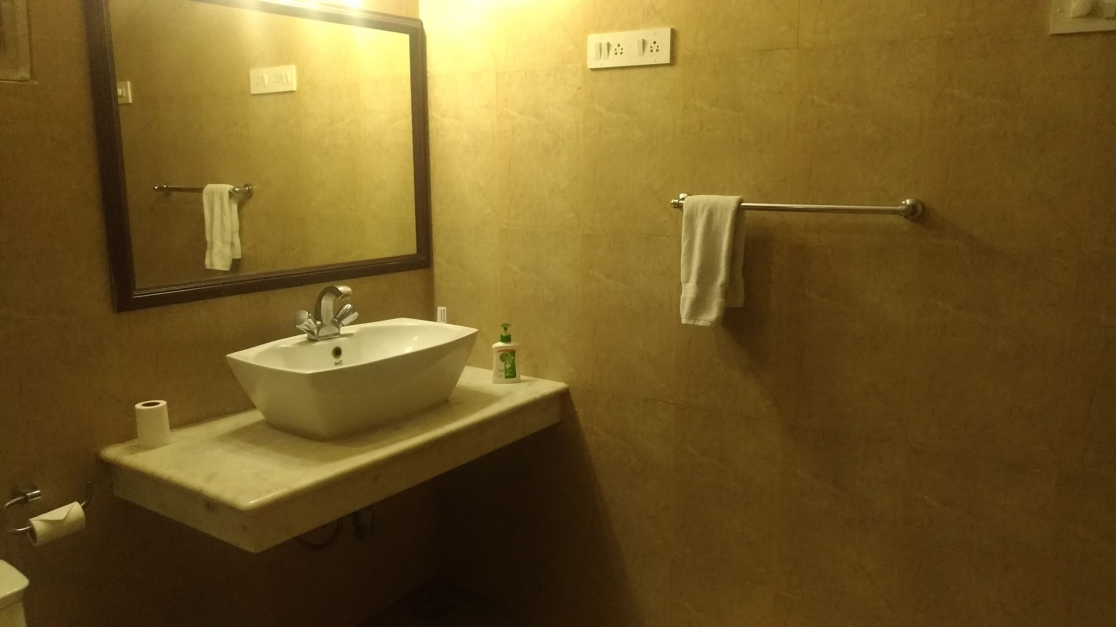 A bathroom with a sink, mirror, towel rack, and a bottle of hand soap.