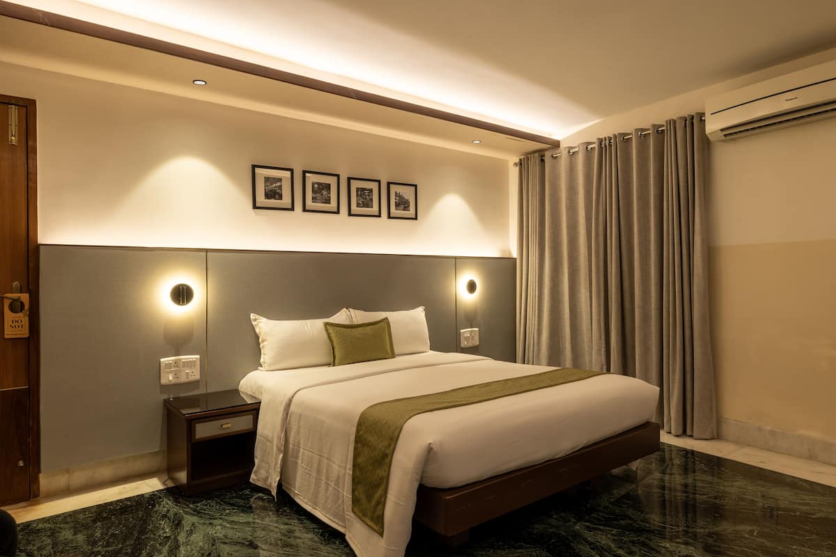 A hotel room with a large bed, bedside tables, a wall-mounted light, and a ceiling-mounted air conditioning unit.