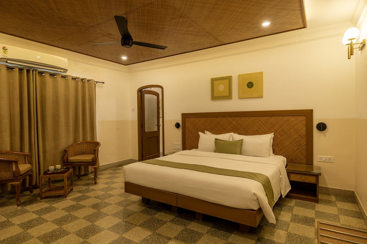 A hotel room with a large bed, two chairs, a small table, a nightstand, and a ceiling fan.
