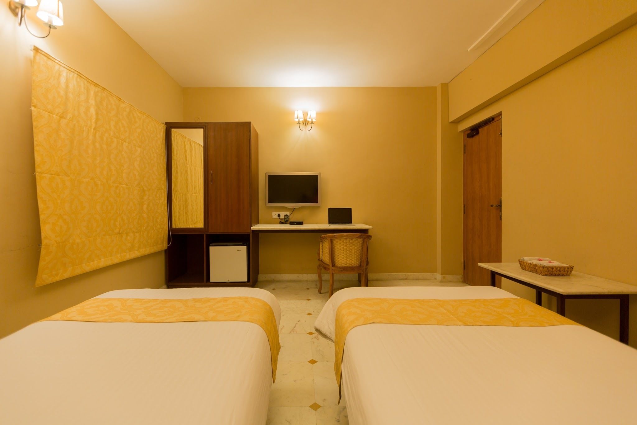 Habitación de hotel con dos camas, un escritorio con computadora, una silla y una mesita con una cesta.