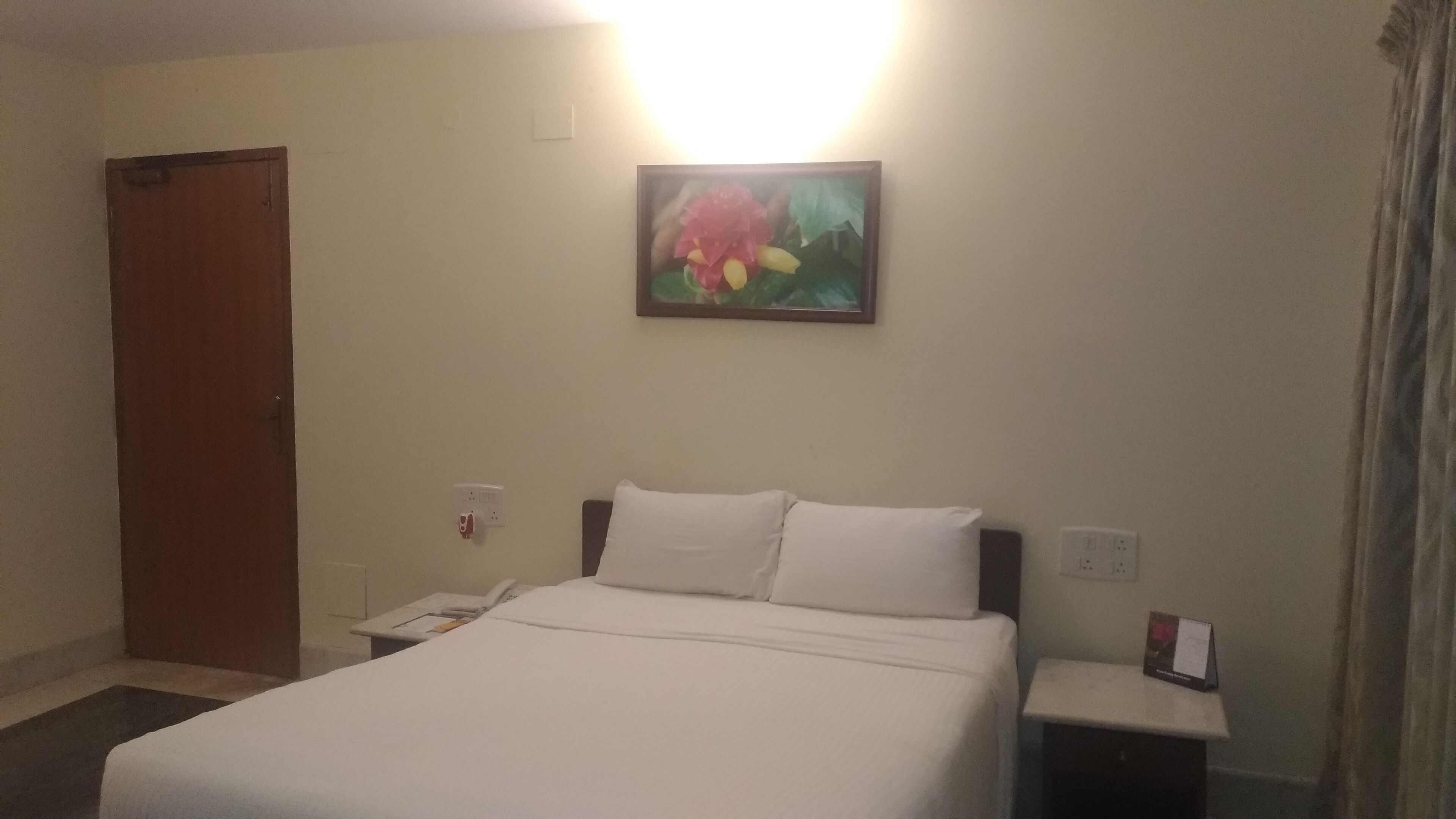 Una habitación de hotel con cama, mesita de noche, teléfono y un cuadro en la pared.