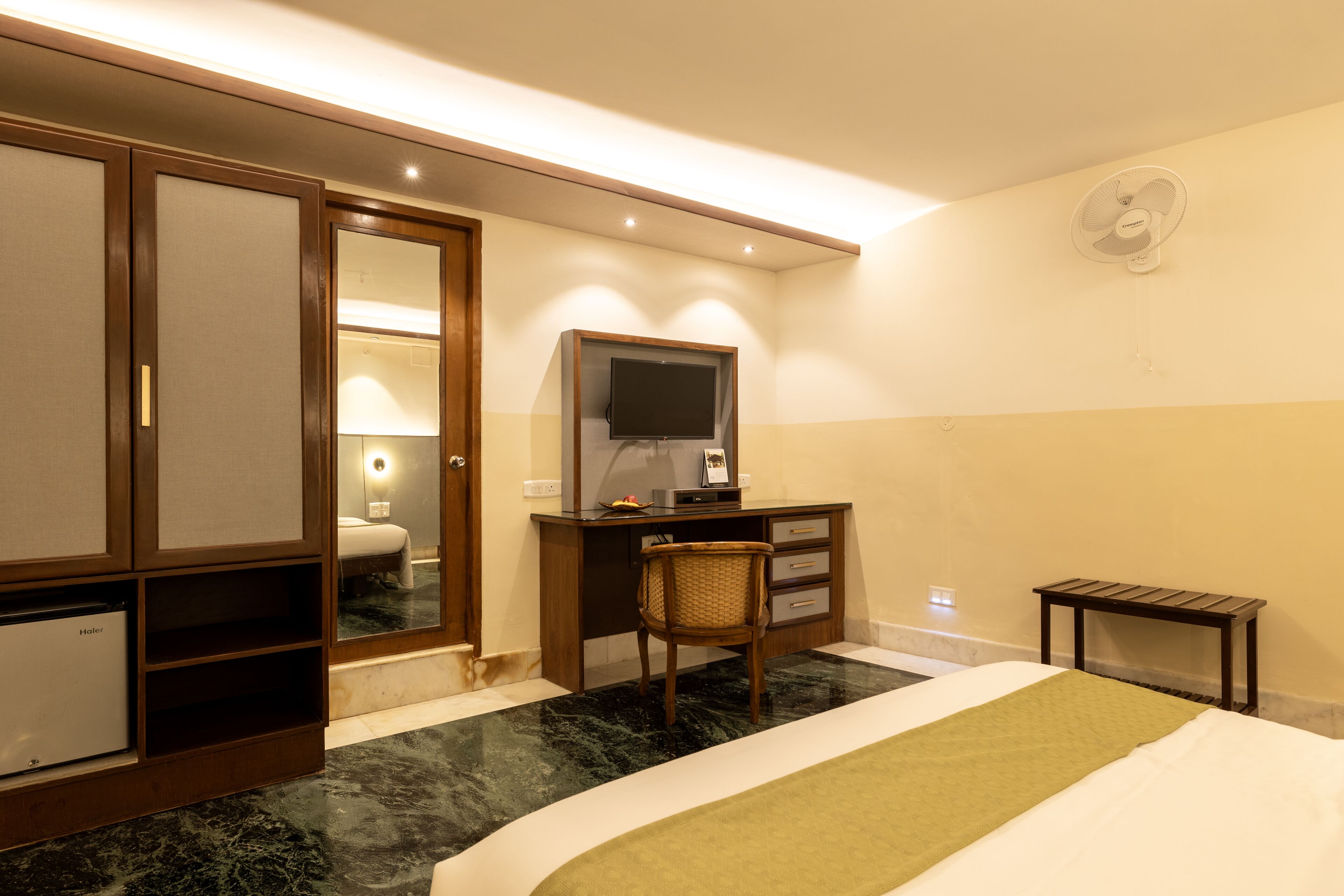 Une chambre d’hôtel comprenant un lit, un bureau avec un ordinateur, une télévision, un petit réfrigérateur et un miroir.