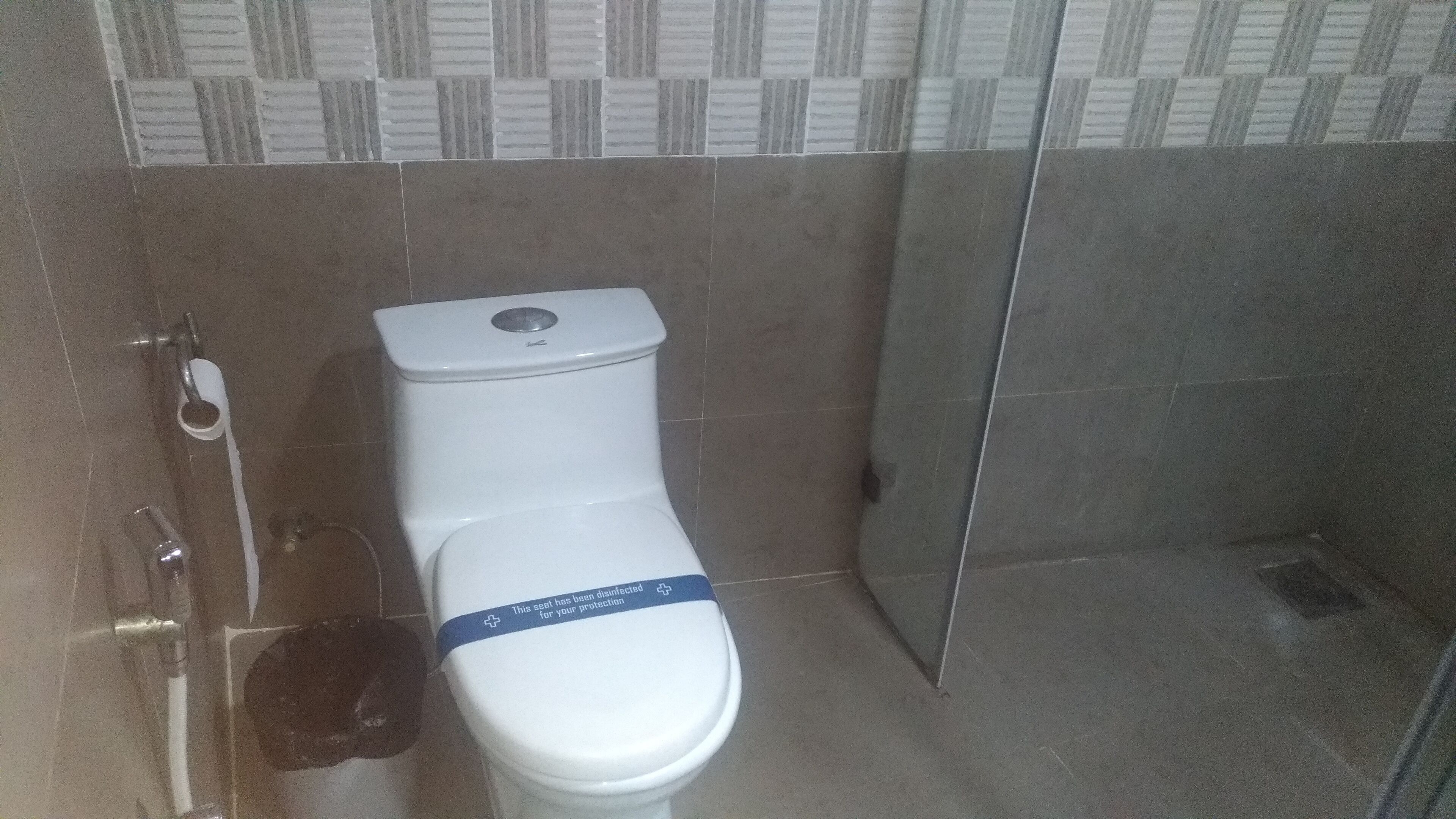 Un inodoro blanco con tapa azul en un baño con paredes de azulejos y zona de ducha.
